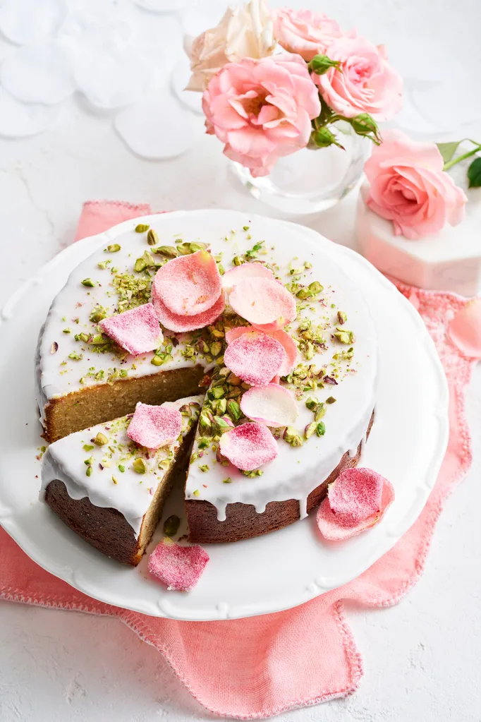 cake with white drip icing and crystallised rose petals on top and pistachio crumb