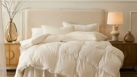 Cosy neutral-toned bedroom featuring a plush white quilt, soft pillows and warm bedside lighting. The quilt is the Greenfirst winter 90/10 goose down quilt in white, available from Pillow Talk.