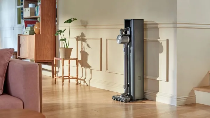 A stick vacuum cleaner in a charging station, standing in a brightly lit living room.