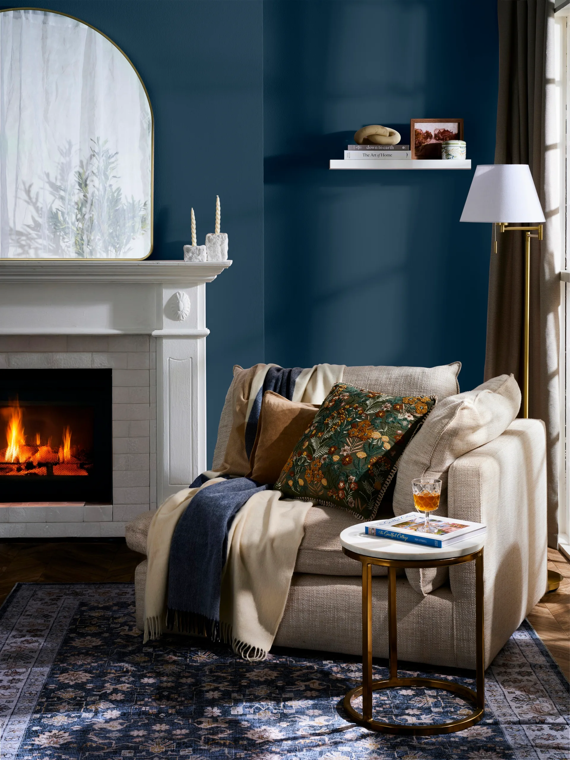 classic cosy nook idea with freedom couch end with blankets draped over it and dark blue walls, fireplace and arched mirror on mantel