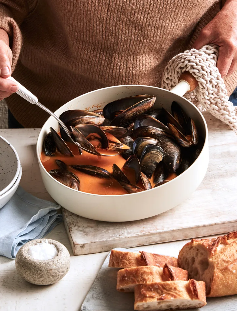 colins fish stew with mussels and leatherjacket in soup in bowl with hands scooping it up and garlic bread to the front