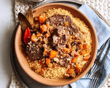 slow cooked beef cheeks with couscous and tomatoes in orange bowl