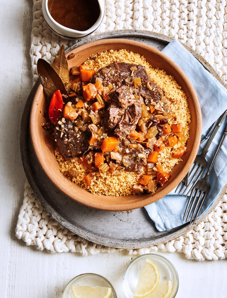 slow cooked beef cheeks with couscous and tomatoes in orange bowl
