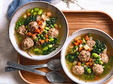 pearl barley stew with chicken dumplings peas and carrots floating in it