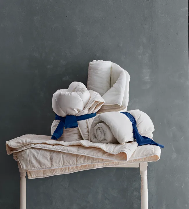 blankets and doonas rolled up on table with a grey background behind it