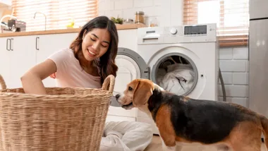 Woman and beagle in a bright laundry area with white appliances and light wood cabinets.