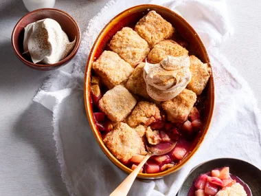 pear and berry cobbler with scones cooked on top in oval tray with spoon sticking out
