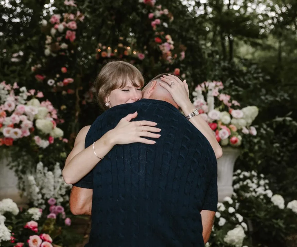 Taylor Swift and Travis Kelce embrace during their engagment surrounded by flowers