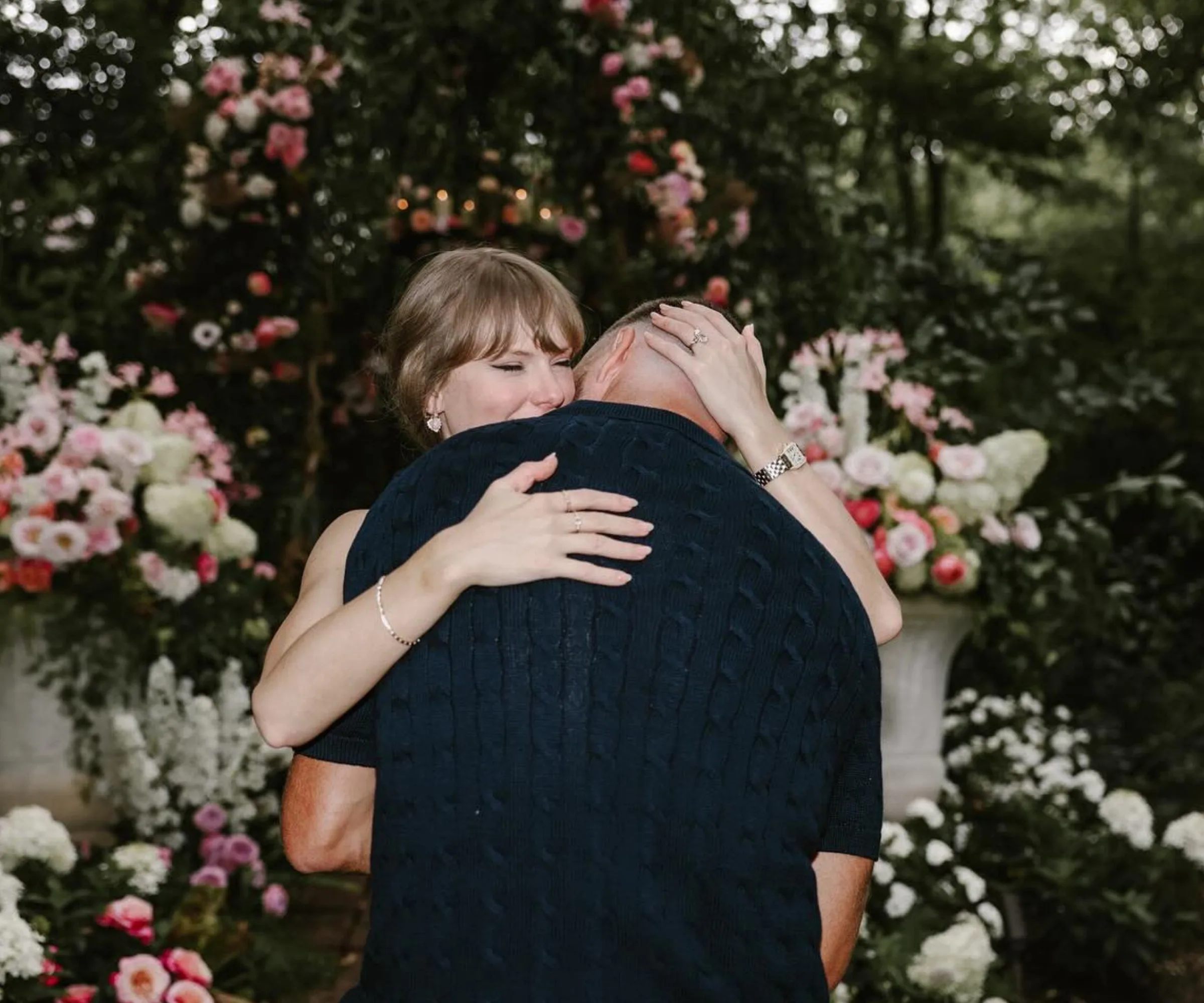 Taylor Swift and Travis Kelce embrace during their engagment surrounded by flowers