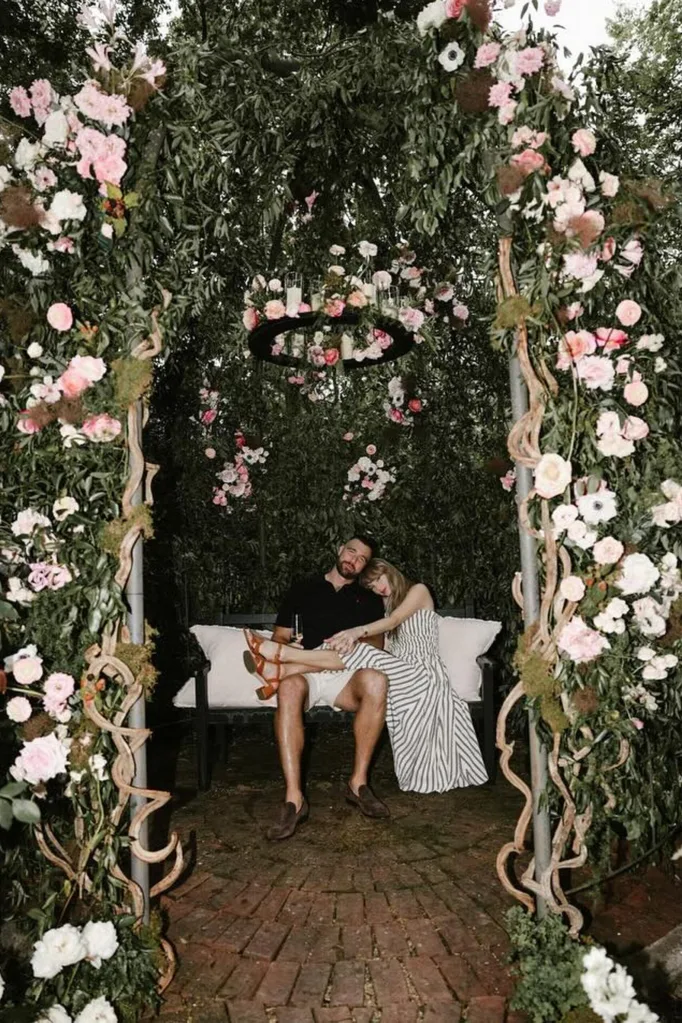 Travis Kelce and Taylor Swift sit beneath a gazebo decorated with flowers and candles for their engagement.