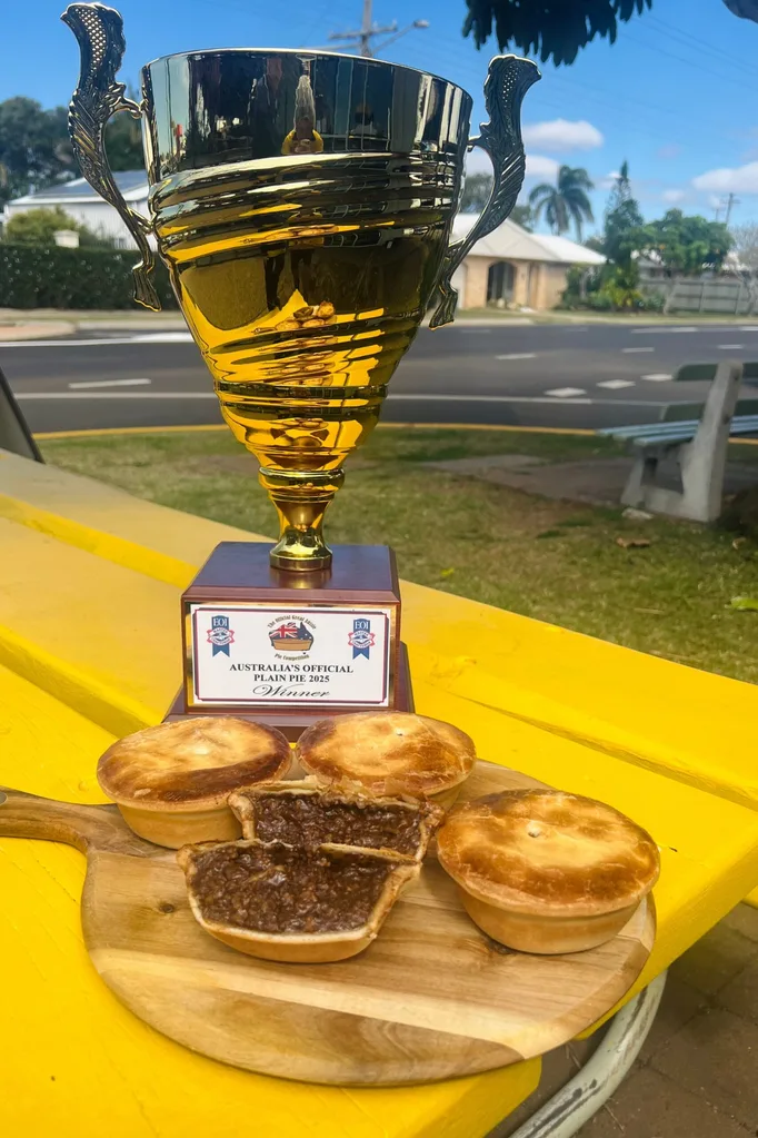 four meat pies on chopping board with one cut open and trphy sitting behind it