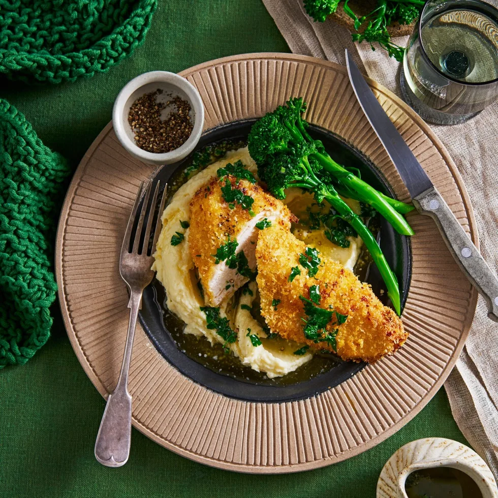 air fryer chicken kiev in brown bowl on blob of mashed potato with broccolini on the side