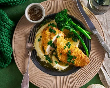 air fryer chicken kiev in brown bowl on blob of mashed potato with broccolini on the side