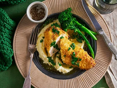 air fryer chicken kiev in brown bowl on blob of mashed potato with broccolini on the side