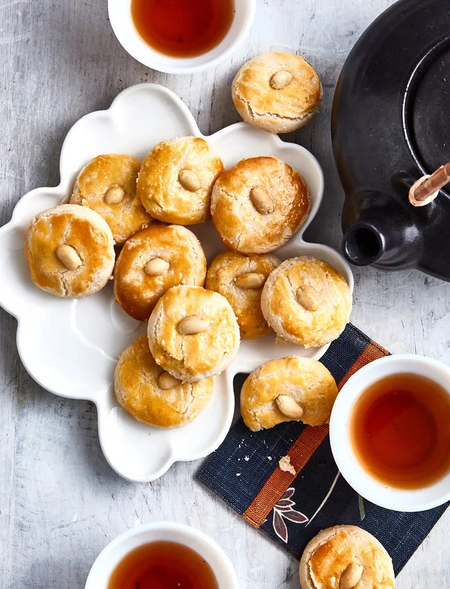 peanut cookies balancing on top of each other on white scalloped plat with cups of tea around it