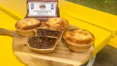 four meat pies on chopping board with one cut open and trphy sitting behind it