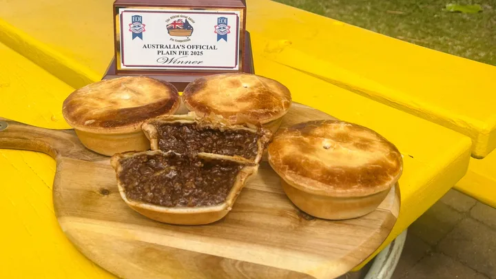 four meat pies on chopping board with one cut open and trphy sitting behind it