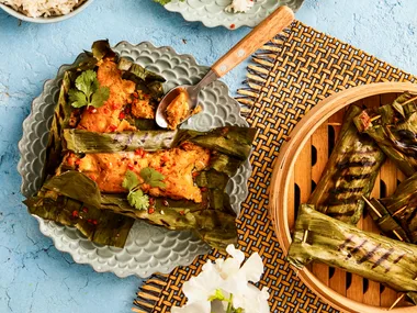 fish cakes wrapped in banana leaves on two separate plates with rice on the side