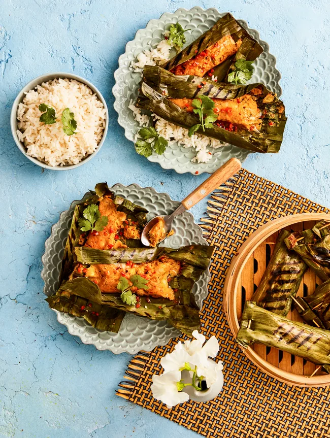 fish cakes wrapped in banana leaves on two separate plates with rice on the side