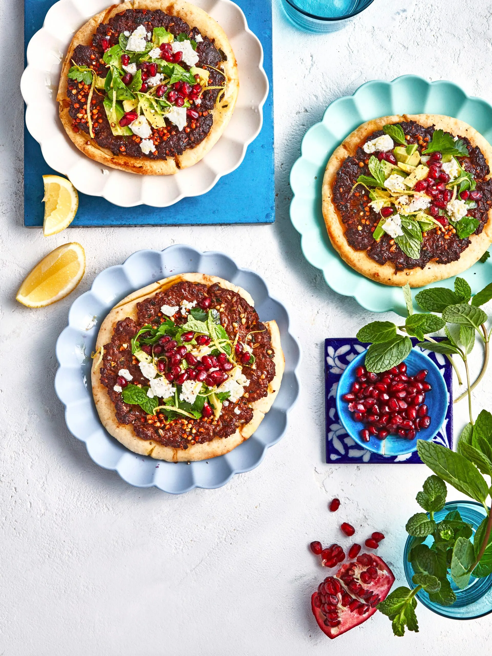pitas with beef smashed into them with mint and pomegranates on top and a bowl of pomegranates on the side
