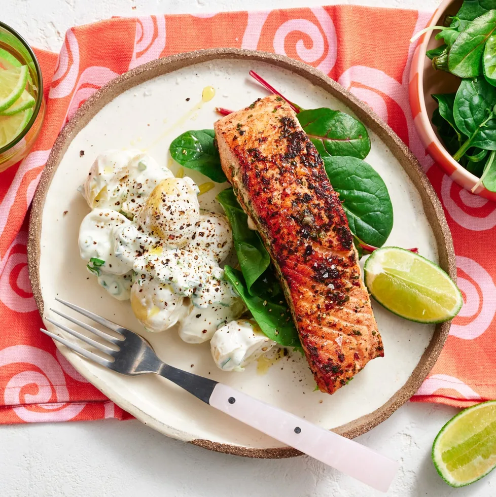 spiced salmon fillet on plate with potato salad next to it on a bed of leaves