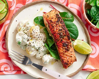 spiced salmon fillet on plate with potato salad next to it on a bed of leaves