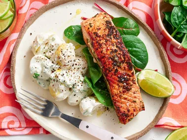 spiced salmon fillet on plate with potato salad next to it on a bed of leaves