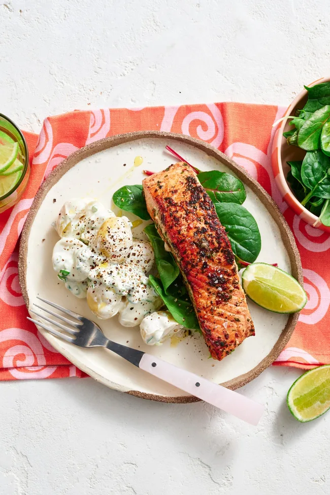 spiced salmon fillet on plate with potato salad next to it on a bed of leaves