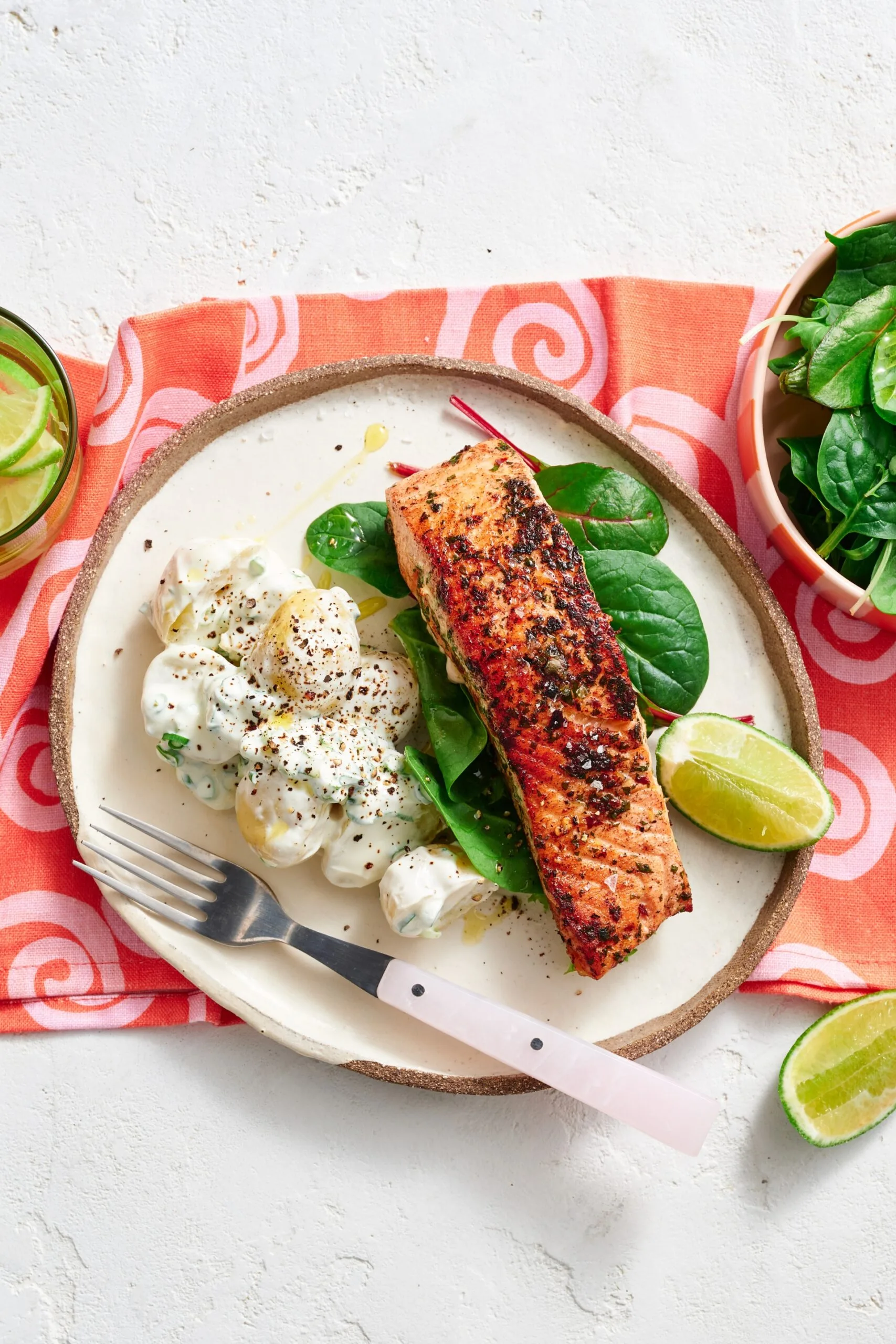 spiced salmon fillet on plate with potato salad next to it on a bed of leaves