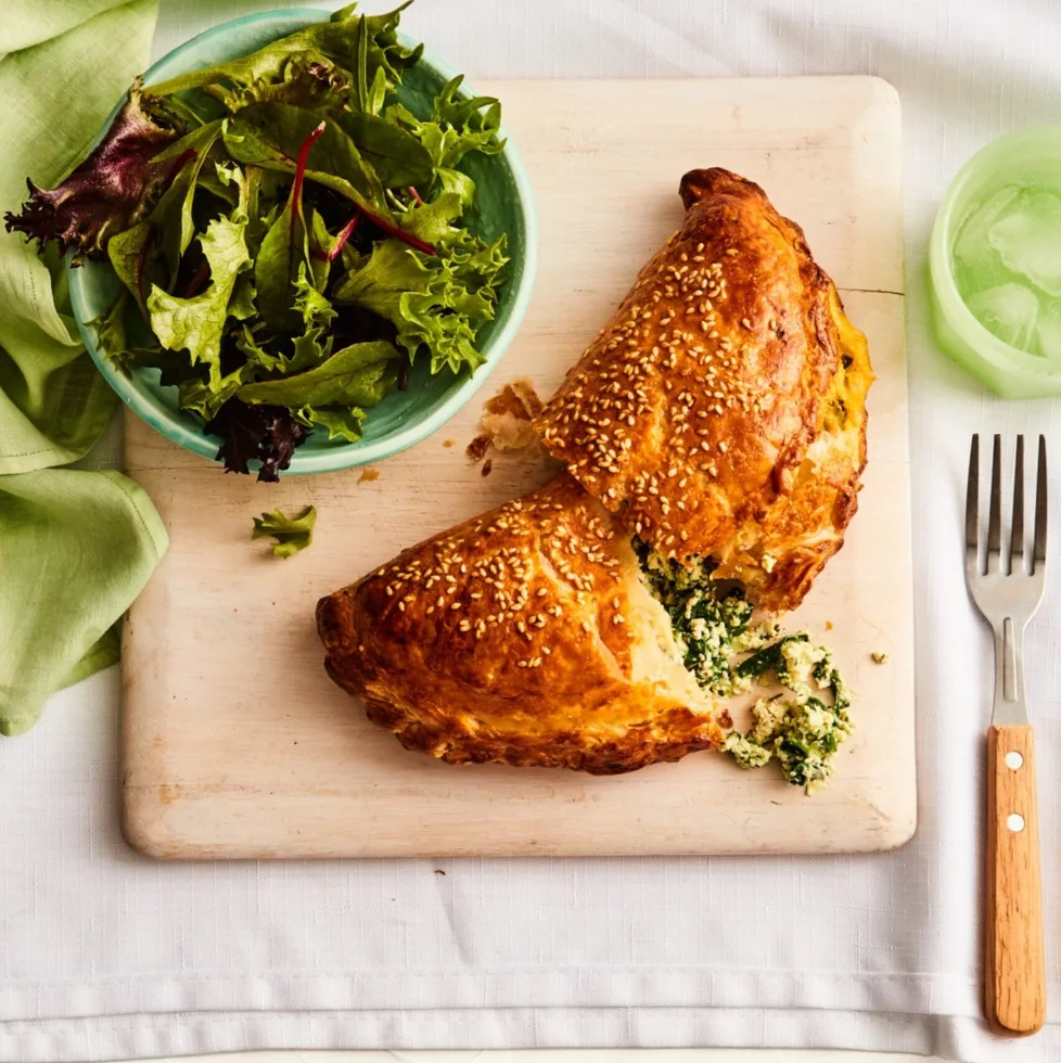 spinach and cheese hand pie cut in half with filling spilling out with fork and bowl of salad on the side