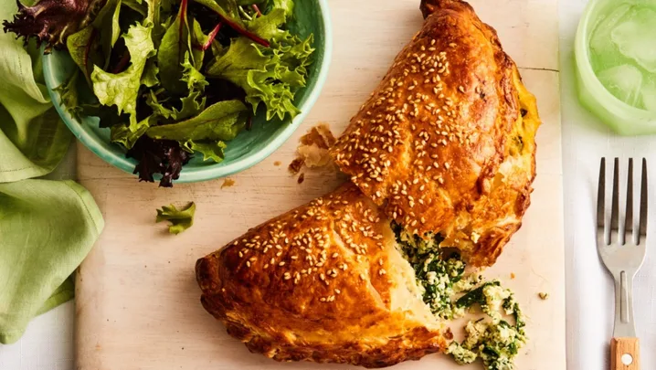 spinach and cheese hand pie cut in half with filling spilling out with fork and bowl of salad on the side