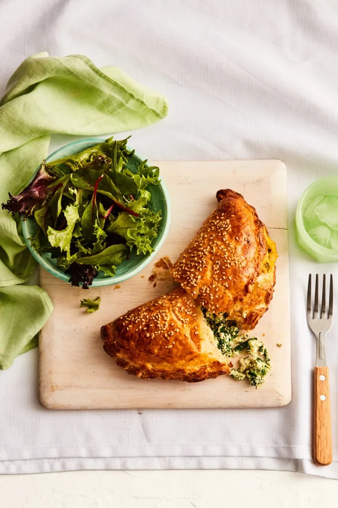 spinach and cheese hand pie cut in half with filling spilling out with fork and bowl of salad on the side