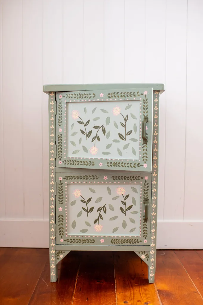floral cabinet painted in sage green and pale green coloured flowers standing against white wall