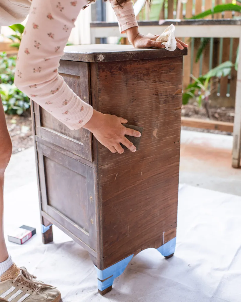 sanding down wooden cabinet with painted blue legs