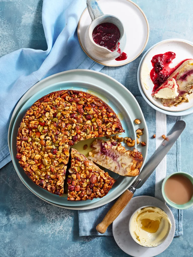 bread and butter cake recipe with cake covered in nuts and seeds with two slices cut to show cross section