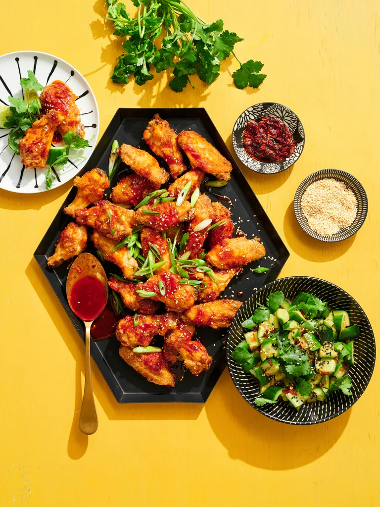 chicken wings on hexagonal plate with spring onions on top and black bowl of smashed cucumber on the side