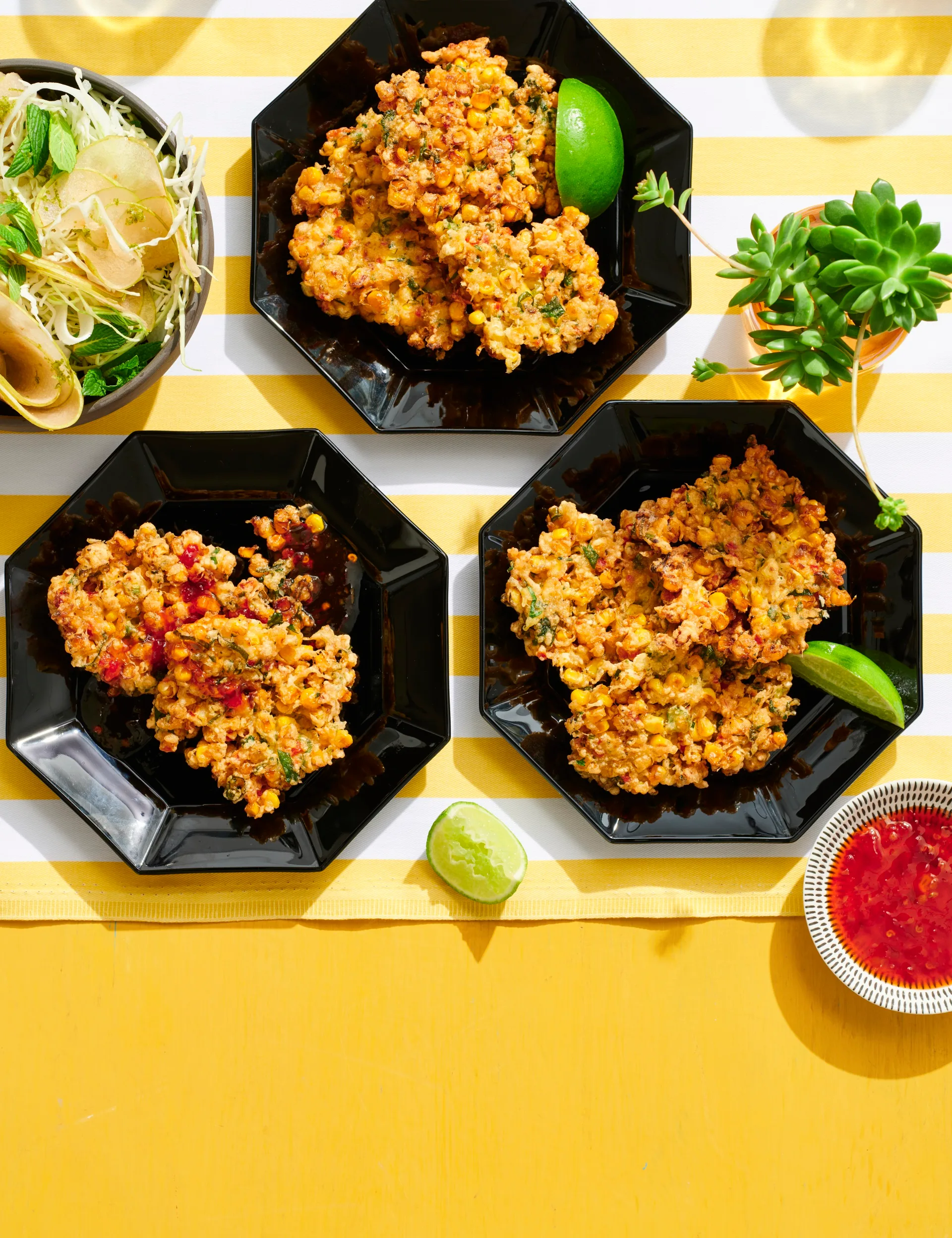 corn fritters in three hexagonal black plates with lime wedges on the side