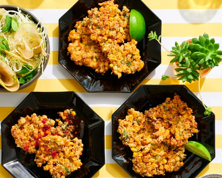 corn fritters in three hexagonal black plates with lime wedges on the side
