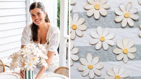 geneva vanderzeil holdinmg a bouquet of white daisy clay flowers in stripy green vase with daisies on stripy tablecloth on the left