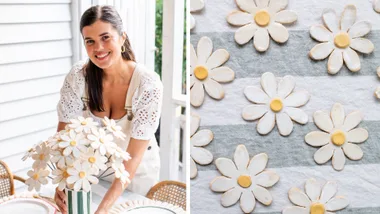 geneva vanderzeil holdinmg a bouquet of white daisy clay flowers in stripy green vase with daisies on stripy tablecloth on the left