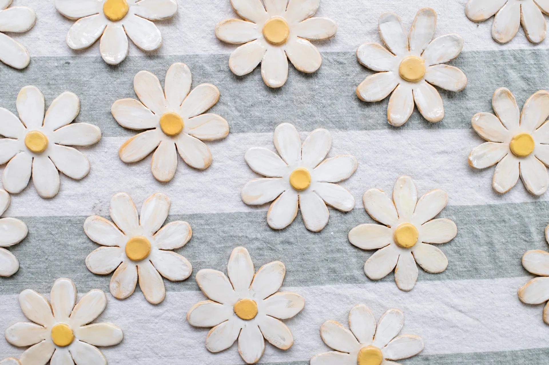 flores de argila acabadas com centro amarelo sobre uma toalha de mesa listrada cinza e branca