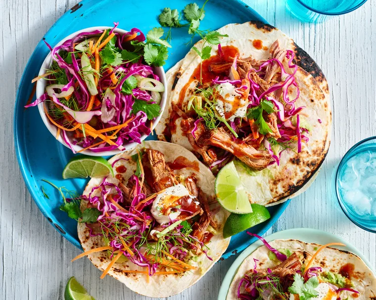 pulled pork tacos open on plate with cabbage slaw on top and in bowl on the side