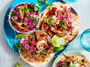 pulled pork tacos open on plate with cabbage slaw on top and in bowl on the side