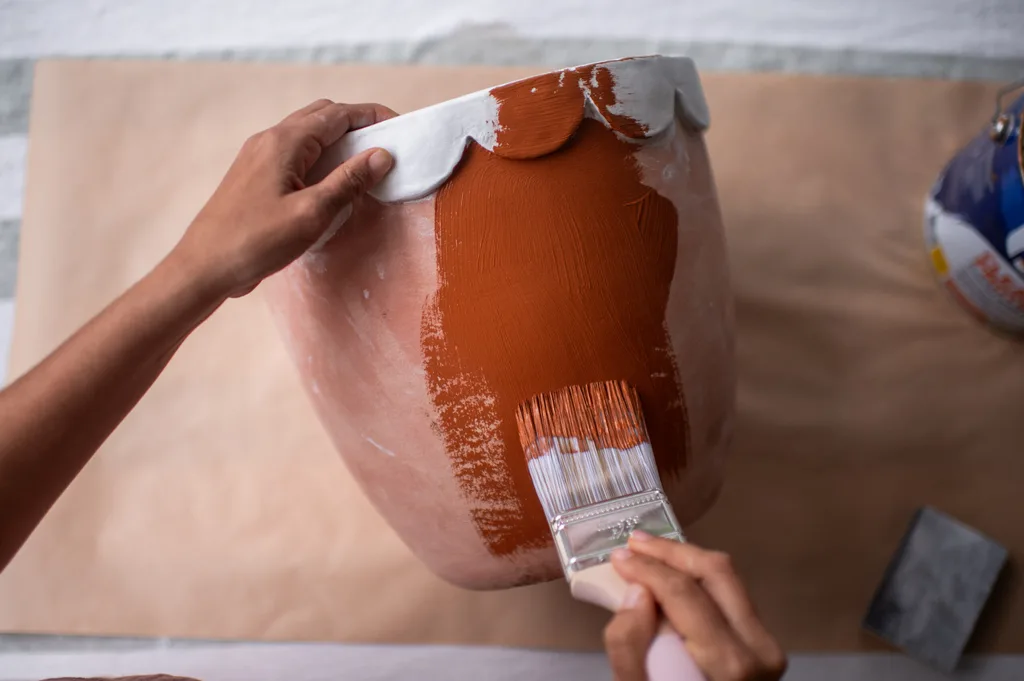 pincel pintando a cor terracota em um vaso e borda recortada feita de argila seca ao ar