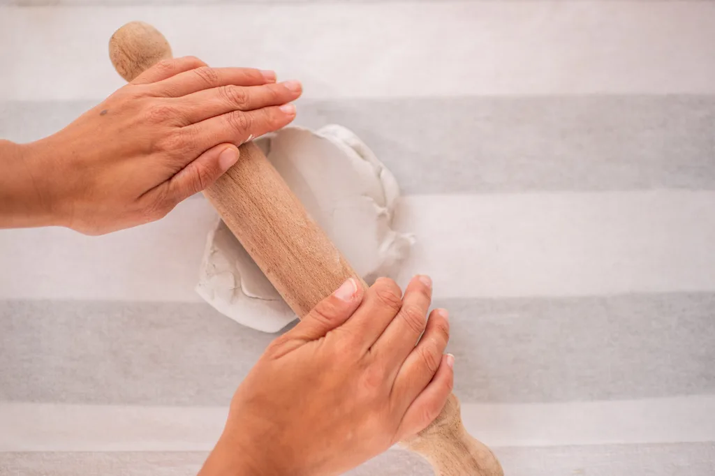 mãos desenrolando argila seca ao ar com rolo