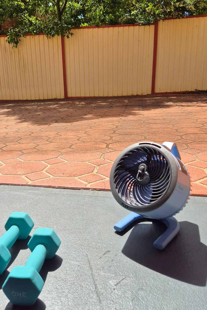 Shark's FlexBreeze Hydrogo portable misting fan on the floor of a garage looking out into a driveway and fence