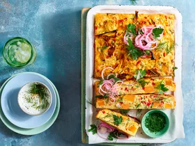 zucchini and pumpkin slice cut up on wooden board with dill yoghurt on the side and glasses of lemonade