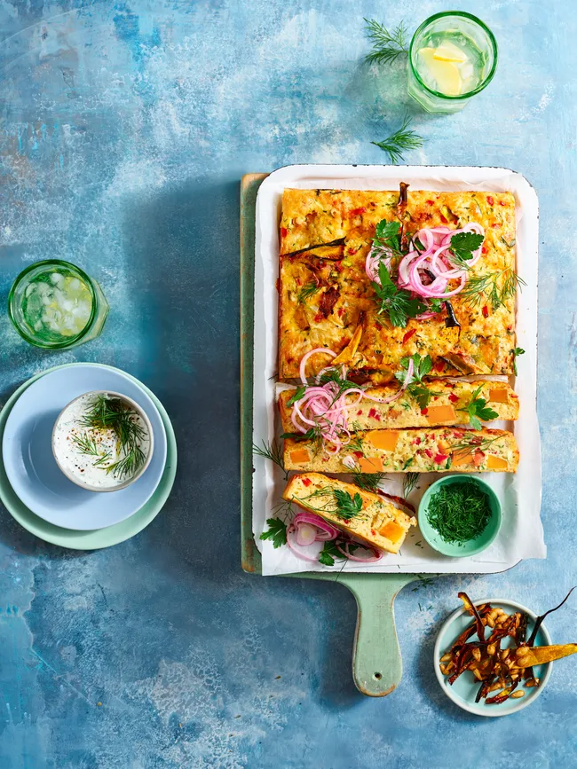zucchini and pumpkin slice cut up on wooden board with dill yoghurt on the side and glasses of lemonade