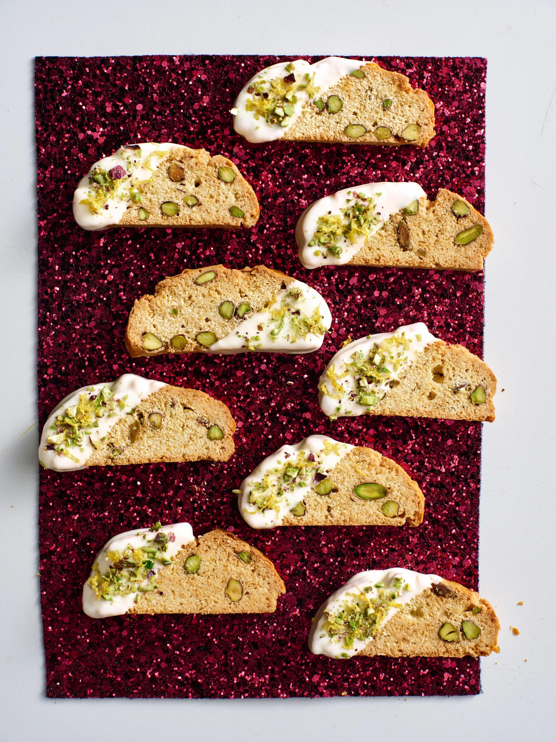 christmas biscotti laid out on red sparkly background with drizlle of white chocolate
