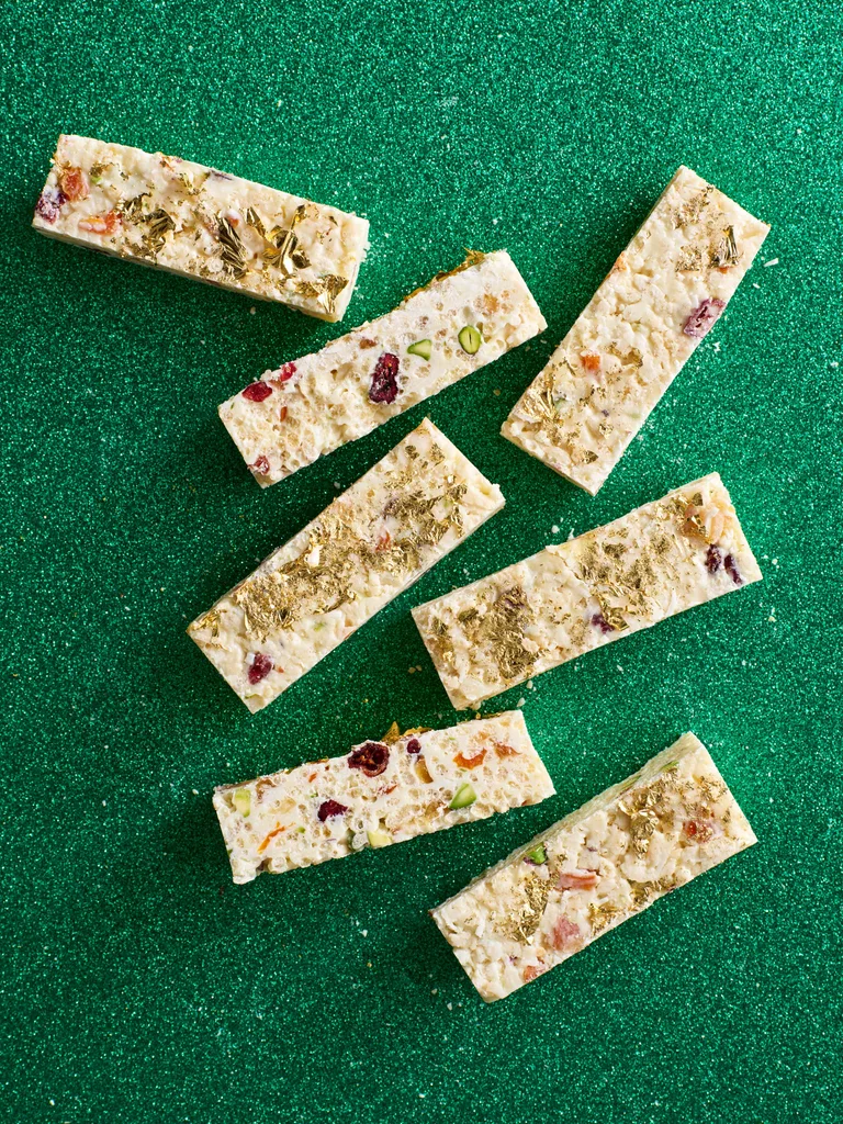 White christmas cut into small rectangular pieces with gold leaf on top and green sparkly background